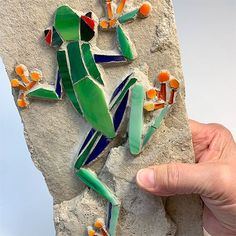 a hand holding up a piece of art that looks like a lizard on a rock