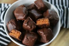 a white bowl filled with chocolate covered pieces of cake pop sitting on top of a wooden table