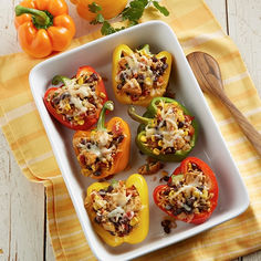 several stuffed peppers in a white casserole dish on a yellow and white towel