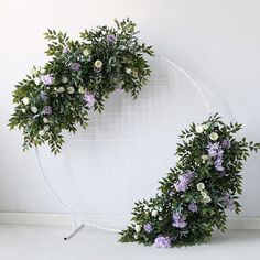 two wreaths made out of branches and flowers on a white wall with a metal stand