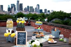 a wooden table topped with lots of desserts and drinks next to a cityscape