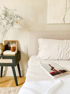 a bed with white sheets and pillows in a bedroom next to a table with a vase on it