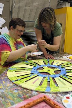 two people sitting at a table working on an art project