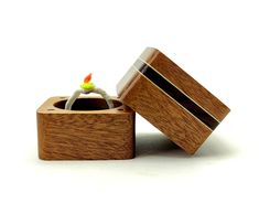 a small wooden box with a ring in it's center and an orange flower sticking out of the top