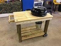 a bbq grill sitting on top of a wooden table next to a metal bucket