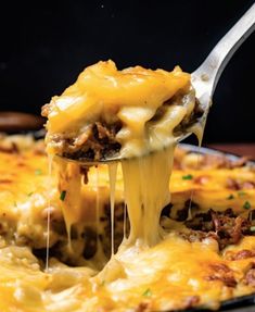 a spoon full of cheese being lifted from a casserole dish with meat and cheese