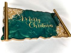 a green and gold merry christmas card with two pens on it, laying next to each other