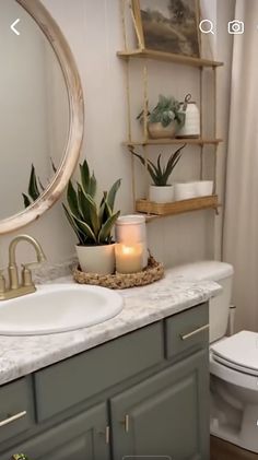 a white toilet sitting next to a bathroom sink under a round mirror with candles on it