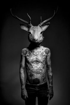 a man with tattoos on his body and deer's head is standing in the dark