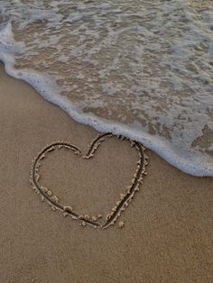 a heart drawn in the sand at the beach with waves coming in and out behind it