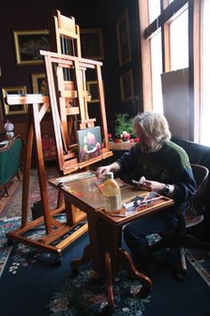 a woman sitting at a table in front of an easel