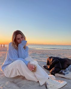 a woman sitting on top of a sandy beach next to a cup of starbucks coffee