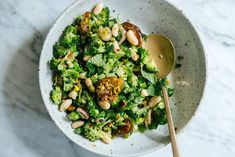 a white bowl filled with broccoli and beans next to a wooden spoon on a marble surface