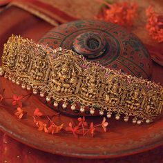 an elaborate gold head piece sits on a red plate with flowers around it and in the background