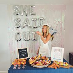 a woman standing in front of a table with food on it and balloons behind her