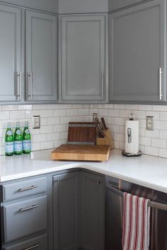 a kitchen with gray cabinets and white counter tops, along with a wooden cutting board