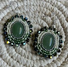 a pair of green and white beaded earrings sitting on top of a woven rug