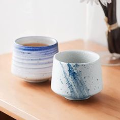 two blue and white cups sitting on top of a wooden table next to a vase with flowers