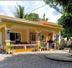 a small yellow and white house with trees in the back ground, surrounded by gravel