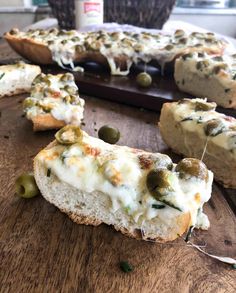 several pieces of bread with cheese and olives on it sitting on a cutting board