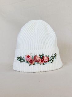 a white knit hat with pink flowers on the front and green leaves on the side