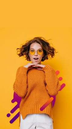 a woman in an orange sweater and white pants poses with her hands on her hips