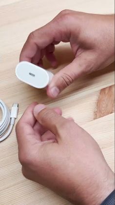 two hands are plugging in and charging an electronic device on a wooden table with wires