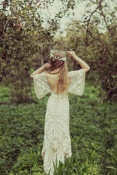 a woman standing in the grass with her back to the camera, wearing a white dress