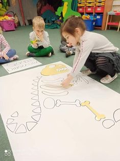 three children are sitting on the floor and playing with paper cutouts in front of them