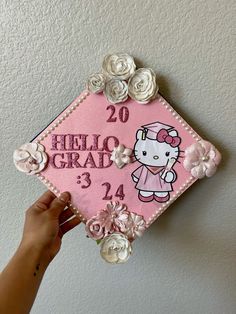 a hand is holding a pink graduation cap with flowers on it and hello kitty in the center