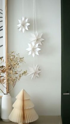 three white paper stars hanging from the ceiling next to a vase with dried flowers in it