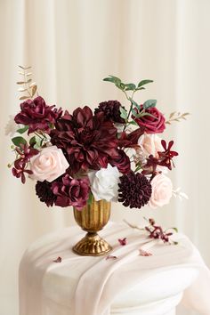 a gold vase filled with flowers on top of a white tablecloth covered table cloth