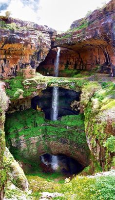 a small waterfall in the middle of a large canyon with green grass and rocks on either side