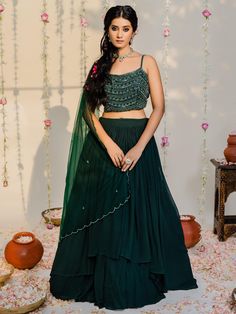 A three-piece bottle green high-low lehenga set from the Redpine Designs collection. This gorgeous bottle green high-low layered flared lehenga is paired with an embroidered blouse. The bottle green color with cutdana, salli, sequin work enhances the graceful georgette lehenga set. The lehenga has beautiful pleats with heavy flare style. The embroidered crop top blouse has intricated embroidery on the straps. The outfit is completed with a bottle green net dupatta with embroidered scalloped edgi Drape Lehenga, Layered Lehenga, Georgette Lehenga, Green Lehenga, Embroidered Crop Tops, Vacuum Storage, Lehenga Blouse, Embellished Blouse