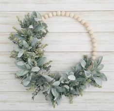 a wreath made out of wood beads and greenery on a white wooden background with copy space