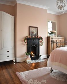 a bedroom with pink walls and white furniture, including a bed in front of a fireplace