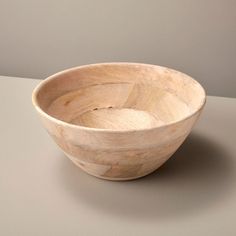 a wooden bowl sitting on top of a table next to a gray wall and floor