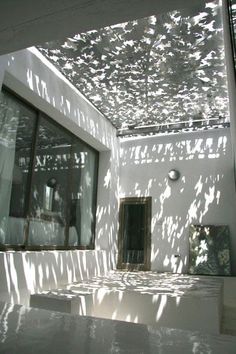 shadows cast on the walls and ceiling of a white building with large windows, in front of an open door