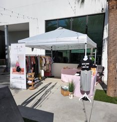 a white tent sitting on top of a sidewalk next to a palm tree in front of a building