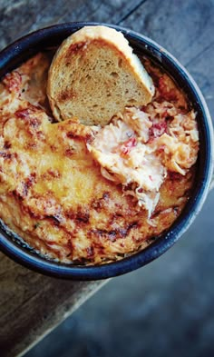 a bowl of food with bread and cheese in it sitting on a wooden table top