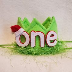 a green felt crown with the word one written in white letters and a red santa hat on top