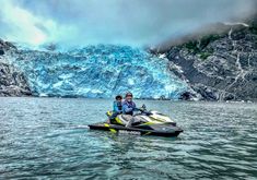 two people on a jet ski in the water near a large ice cave and glacier