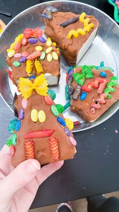 a person holding up a piece of cake decorated to look like a gingerbread house