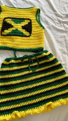 a crocheted green and yellow outfit is laying on a white sheet with a pair of scissors next to it