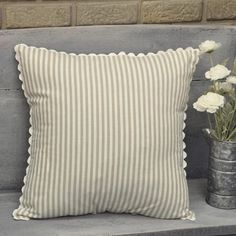 a striped pillow sitting on top of a wooden bench next to a vase with flowers