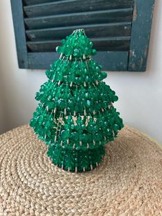 a green beaded christmas tree sitting on top of a straw hat