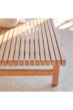 a wooden bench sitting on top of a rug next to a white vase and bowl