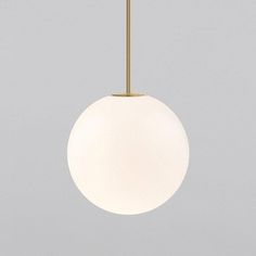 a white ball hanging from a brass colored light fixture on a gray wall with a grey background