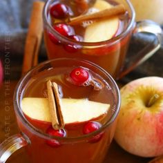 two mugs filled with apple cider and cinnamon stick garnished with apples