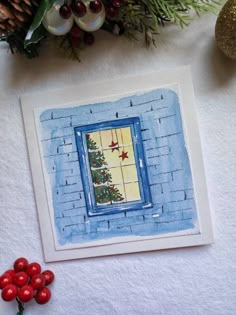 a card with a christmas tree in the window and holly berries on the table next to it